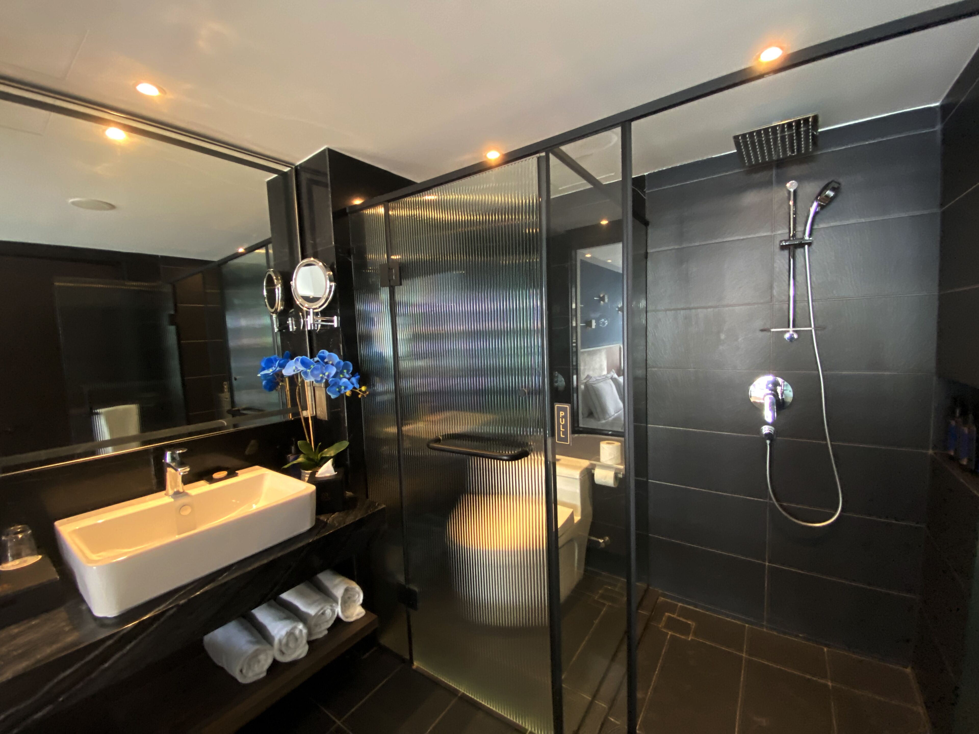Un baño moderno con cabina de ducha de vidrio, un espejo grande y un lavamanos con toallero.