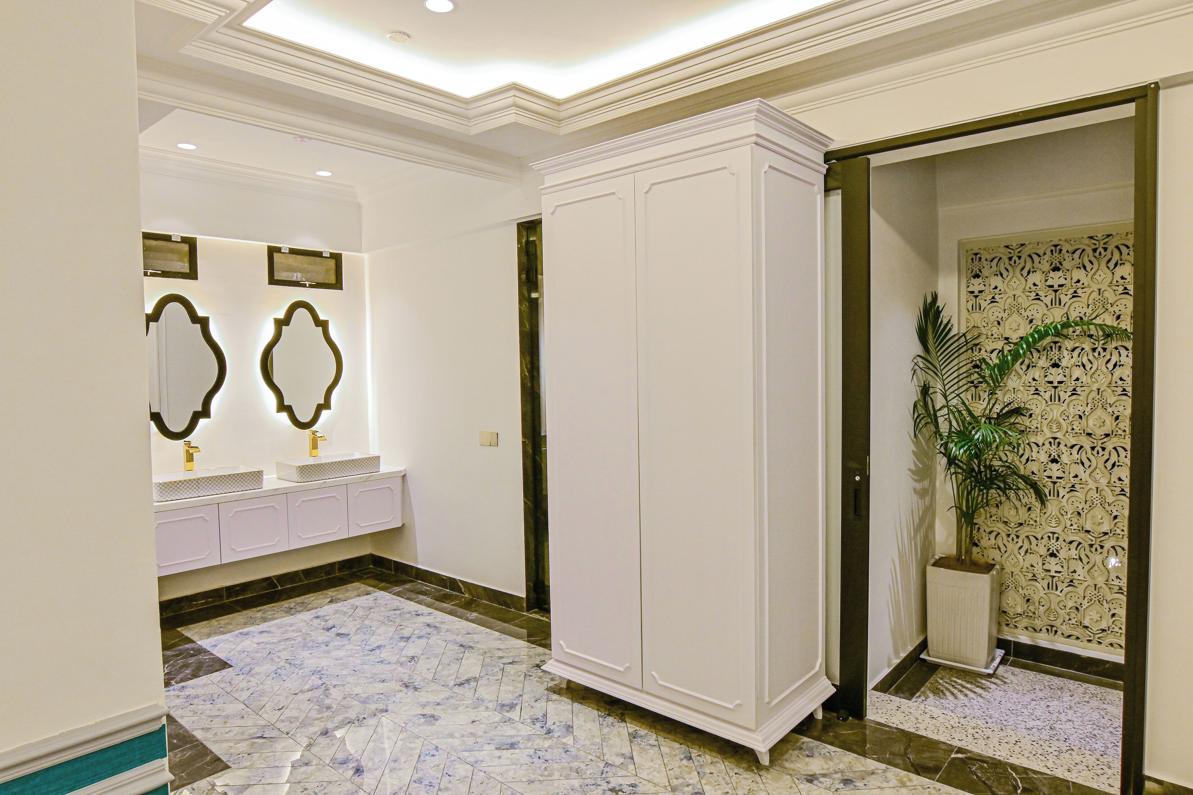 A hotel lobby with a marble floor, a large white wardrobe, a potted plant, and a decorative wall.