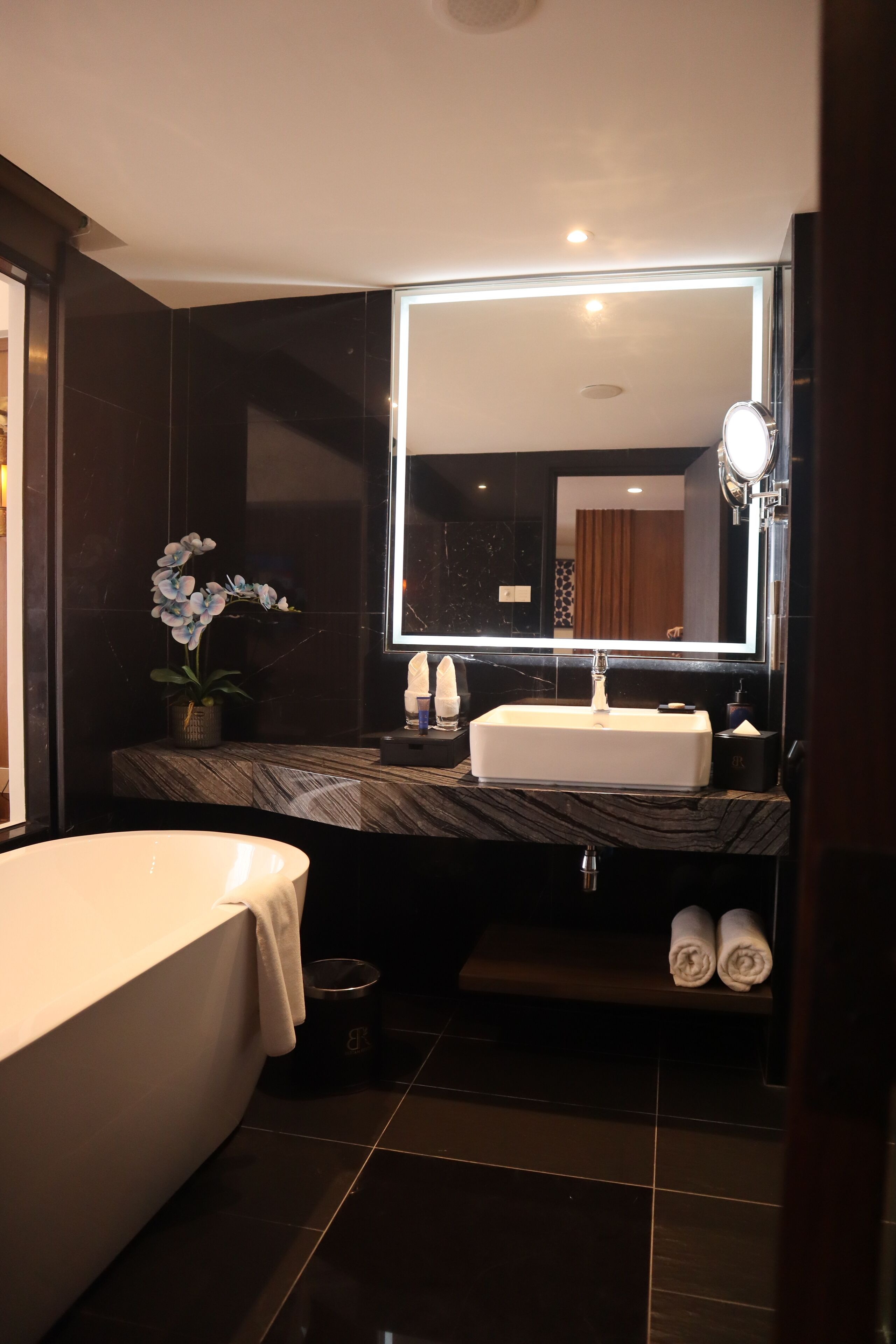 Une salle de bain moderne avec une grande baignoire, un comptoir en marbre, un lavabo, un miroir et une orchidée en pot.