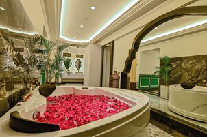 A luxurious bathroom with a large bathtub filled with rose petals, marble walls, and modern decor.