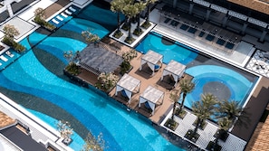 Vista aérea de un hotel con múltiples piscinas, tumbonas y palmeras.