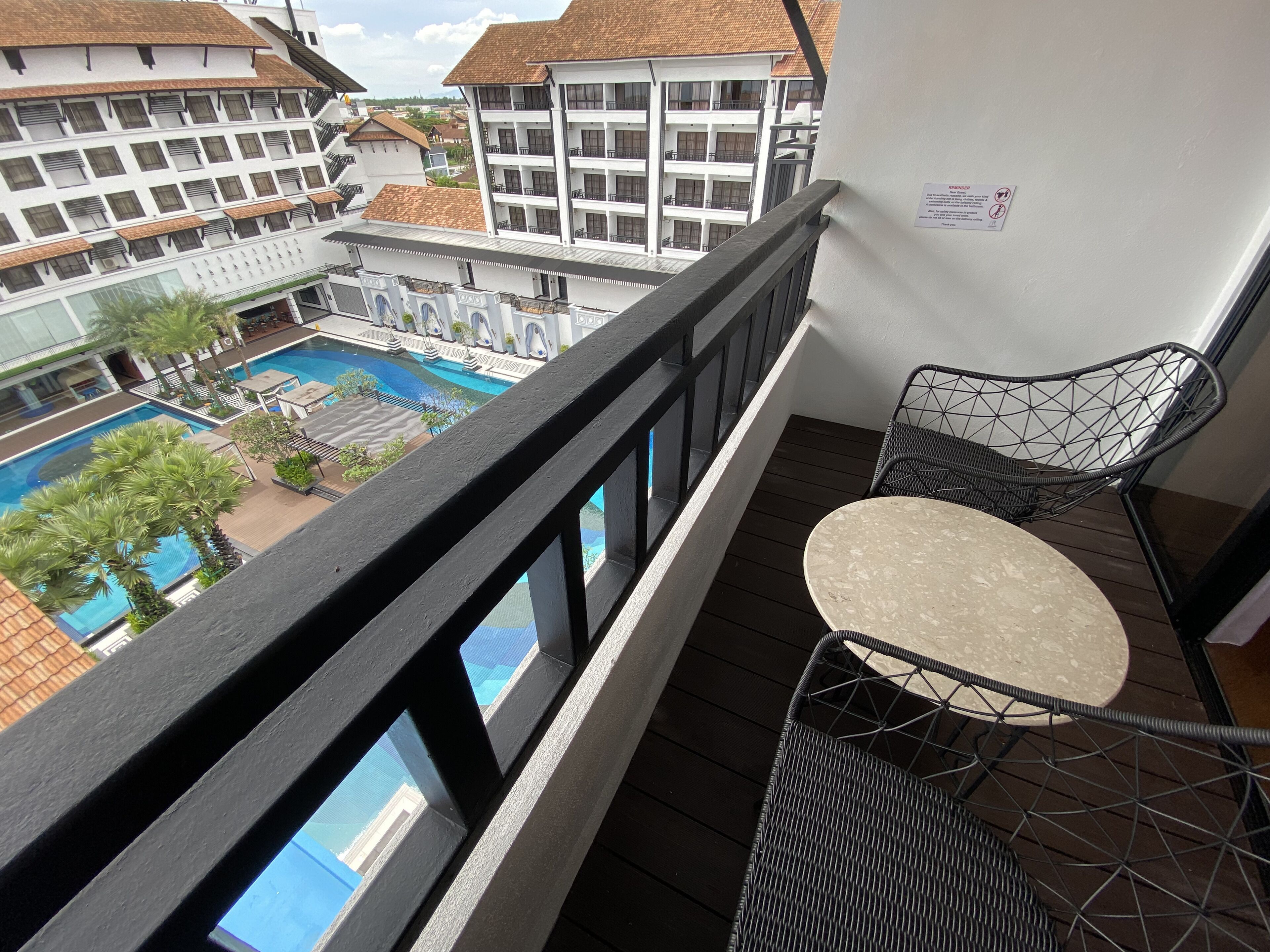 En balkon med udsigt over en swimmingpool og hotelbygninger.