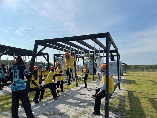 Un grupo de personas participa en una actividad al aire libre, posiblemente un circuito de cuerdas, con cielo despejado y zona de césped al fondo.