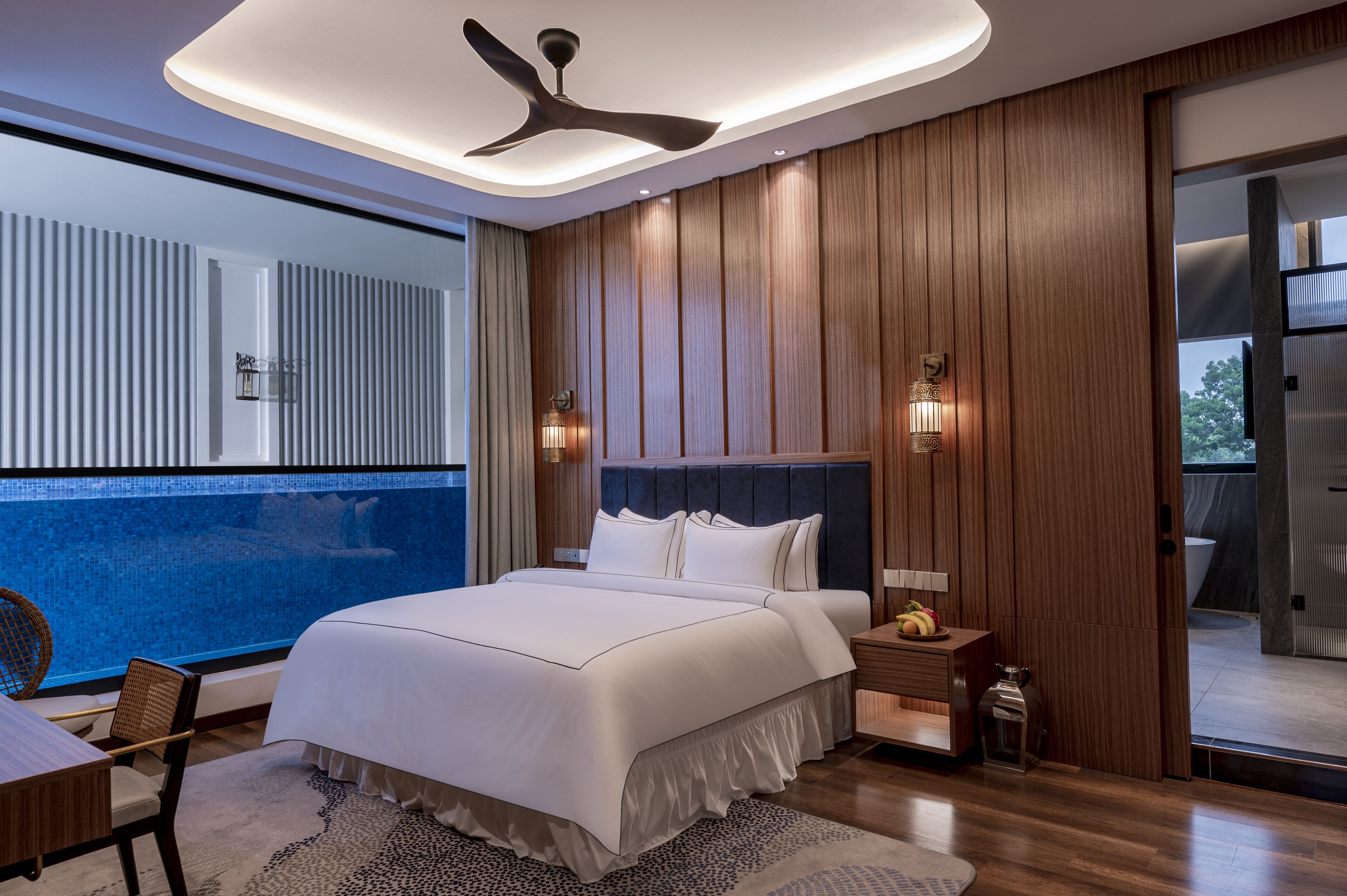 Un dormitorio moderno con una cama grande, paneles de madera, ventilador de techo y vista a una piscina.