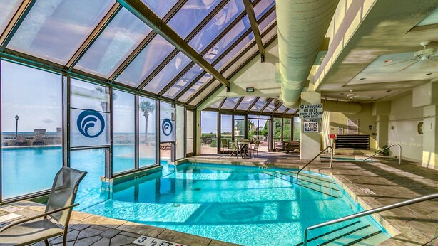 An indoor swimming pool with clear glass walls, a view of the ocean, and a lifeguard sign.