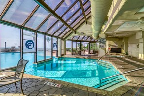 An indoor swimming pool with clear glass walls, a view of the ocean, and a lifeguard sign.