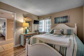 A bedroom with a bed, a dresser, a TV, and a painting on the wall.