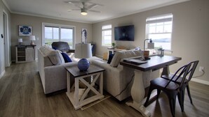 A living room with a sofa, a coffee table, a TV, and a dining area with a table and chairs. - Pet Friendly, 2nd Floor, 2 BD, 2 BA Condo w/ Bayside Views, Steps to Pool, Tennis, Biking, and More! (Ocean View)