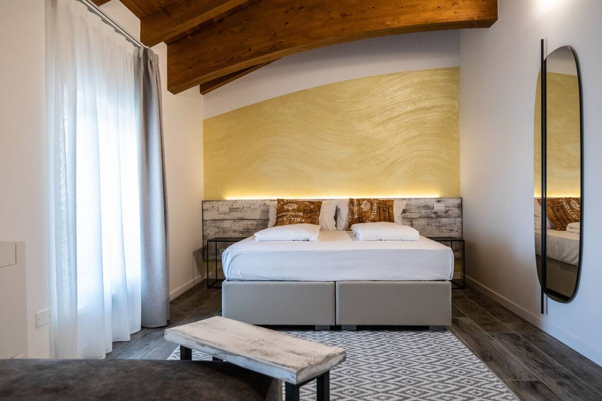 Ein Schlafzimmer mit einem Bett, Nachttischen, einer Bank, einem großen Spiegel und einem gemusterten Teppich.