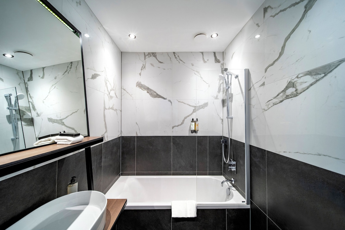 A modern bathroom with a freestanding bathtub, a glass shower enclosure, and marble walls.