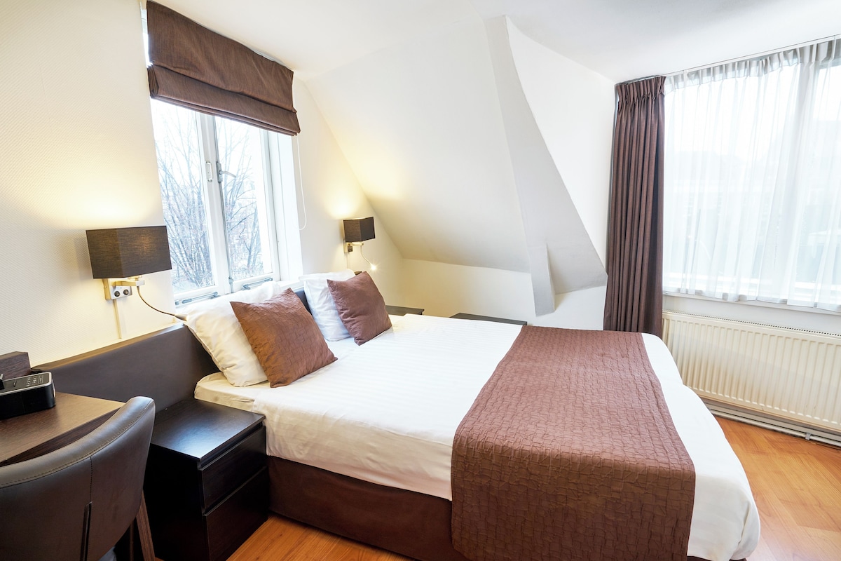 A hotel room with a bed, bedside tables, a desk, and a lamp.