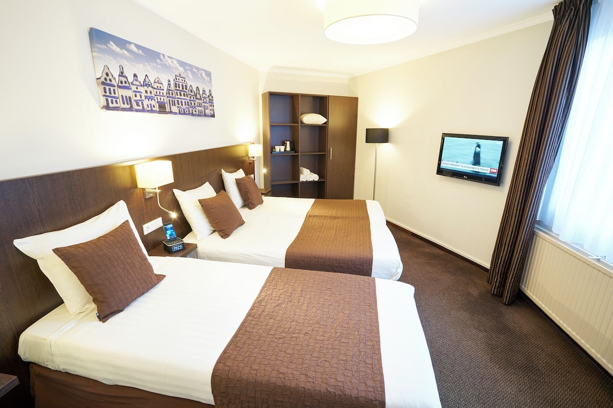 A hotel room with two beds, a television, a painting, and a wardrobe.