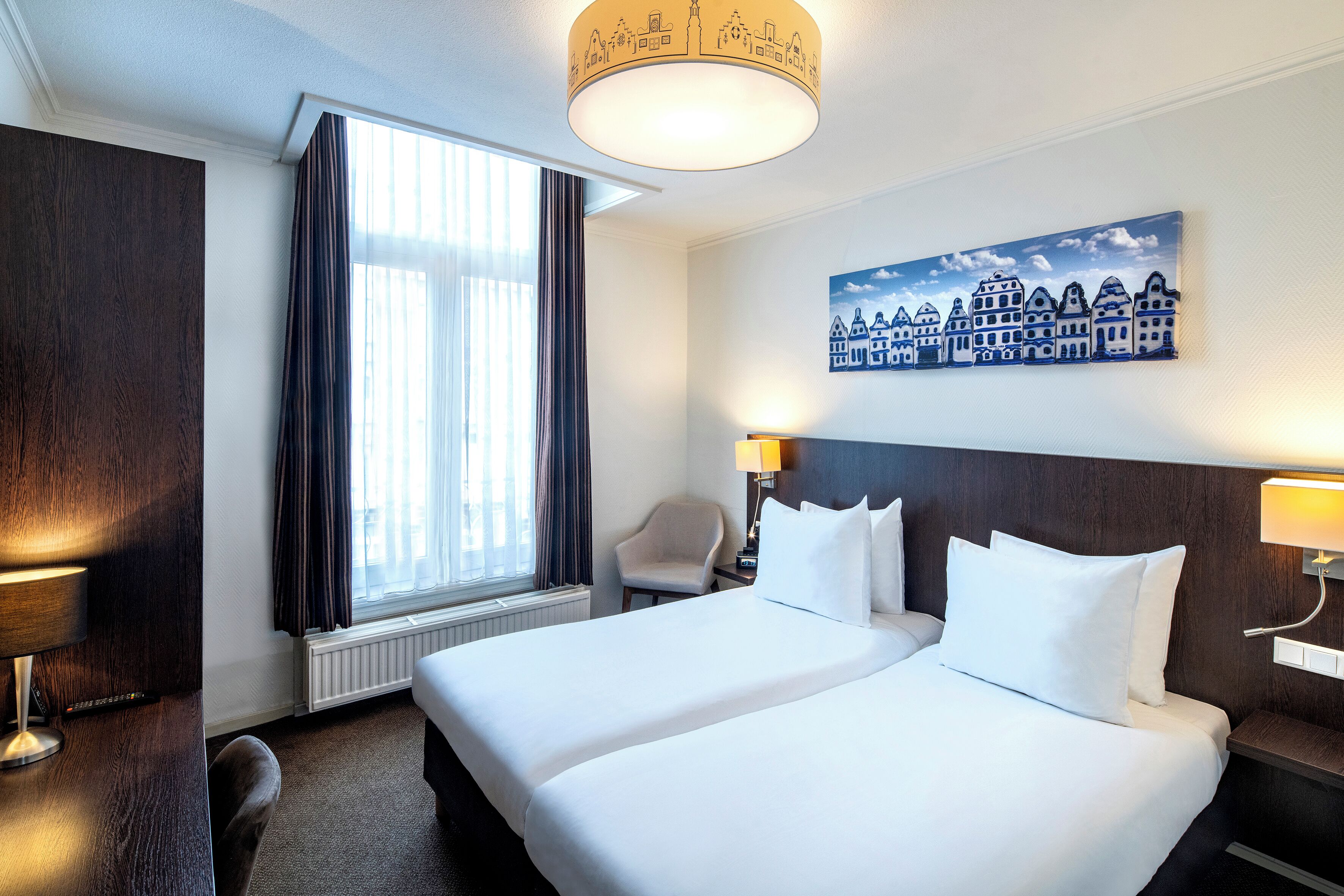 A hotel room with a large bed, a chair, a desk, and a window with curtains.