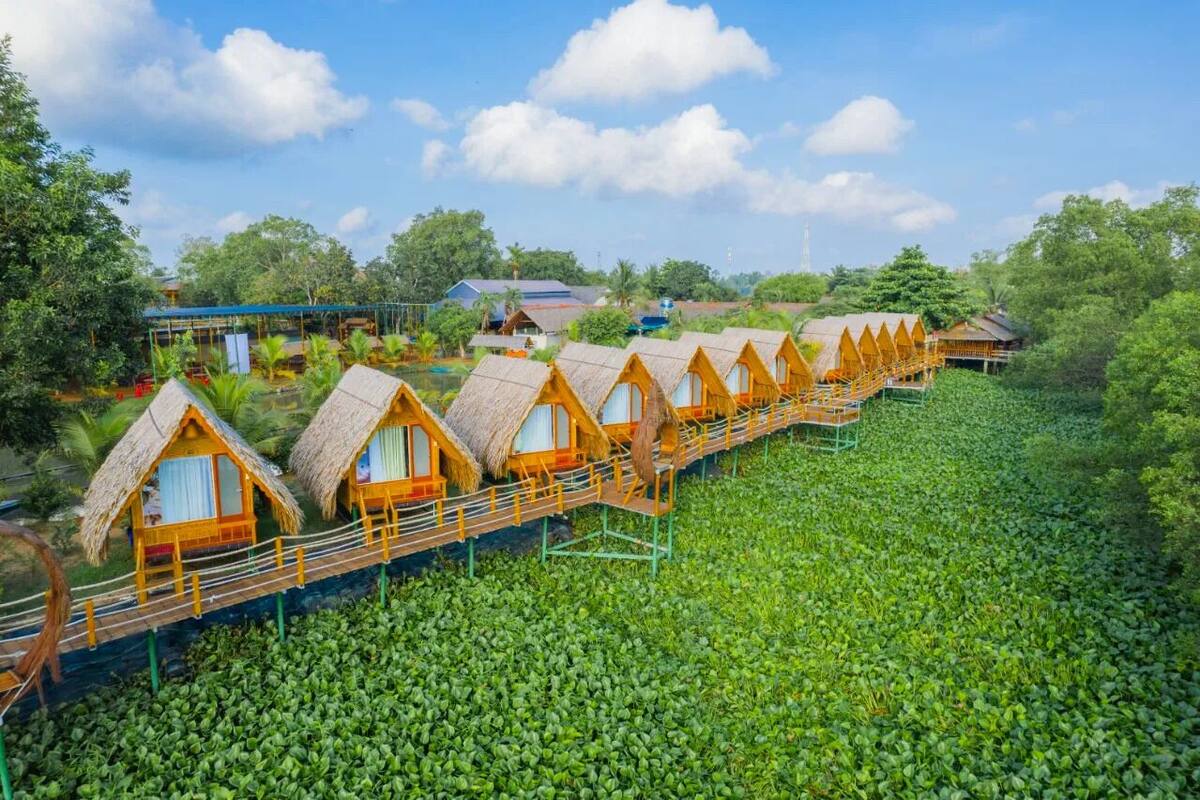 A row of thatched-roof cottages with a wooden walkway connecting them, set in a lush green landscape.