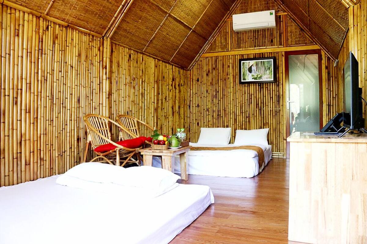 A bamboo-themed room with two beds, a small table with a basket of fruit, and a TV on a wooden desk.