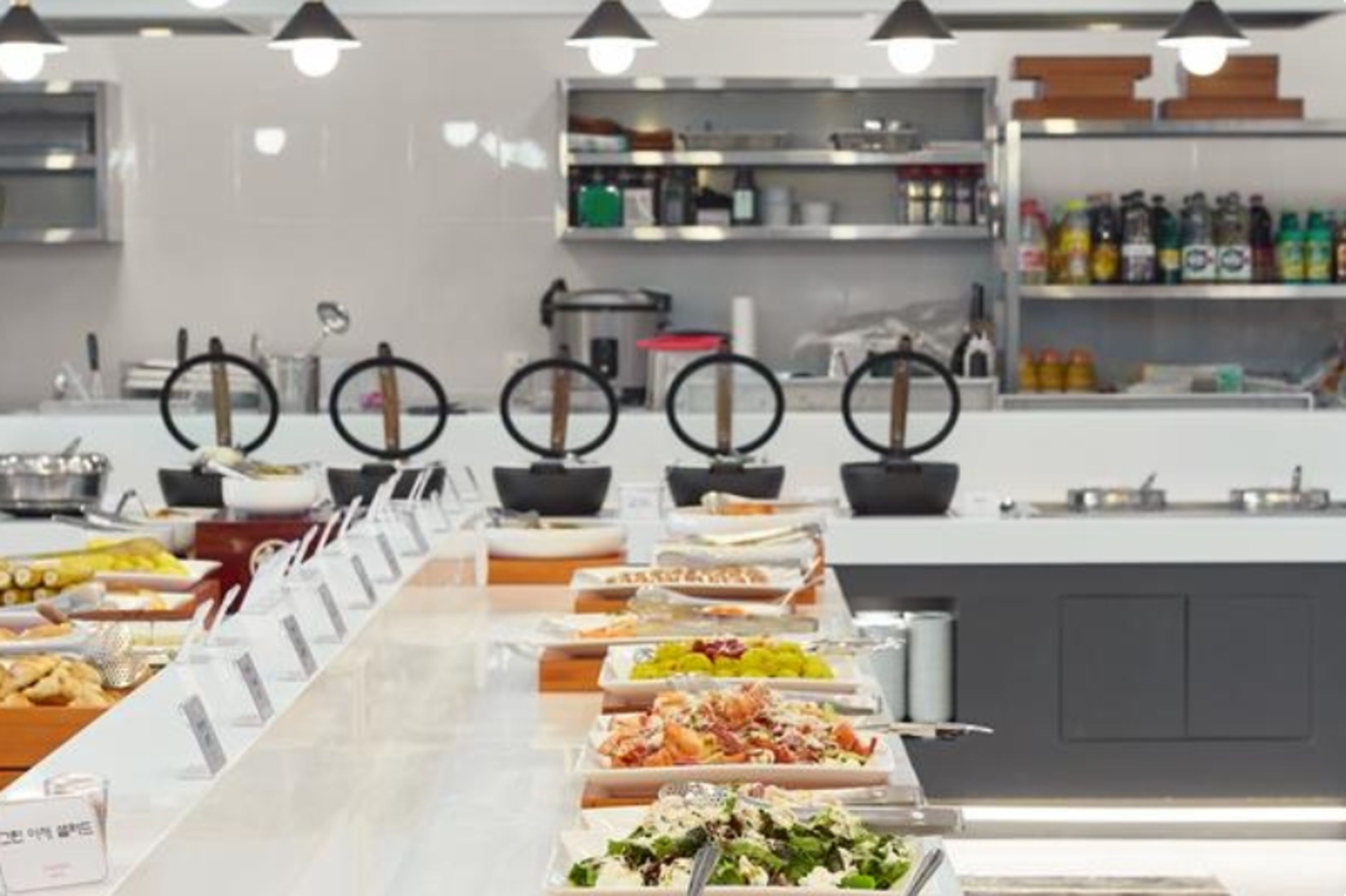 Montaje tipo bufé con diversos alimentos y una zona de cocina al fondo.