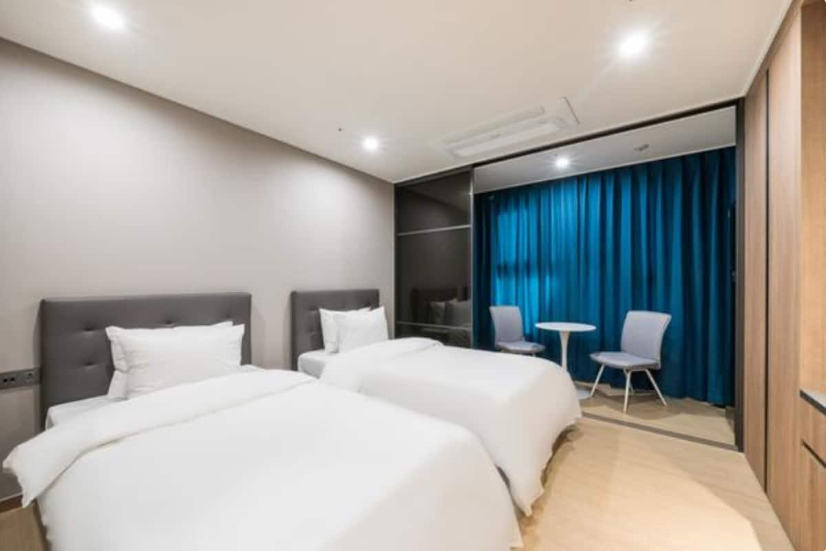 Ein Hotelzimmer mit zwei Betten, einem Schreibtisch, einem Stuhl und einem blauen Vorhang.