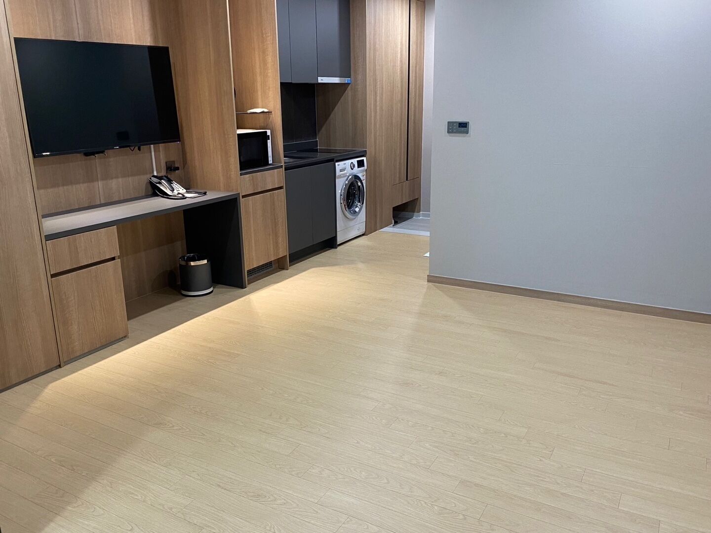 A modern kitchen with a flat-screen TV, microwave, washing machine, and a small trash bin.