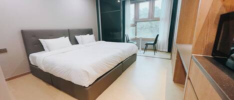 A modern bedroom with a large bed, a small table, two chairs, and a view of the outdoors through a window.