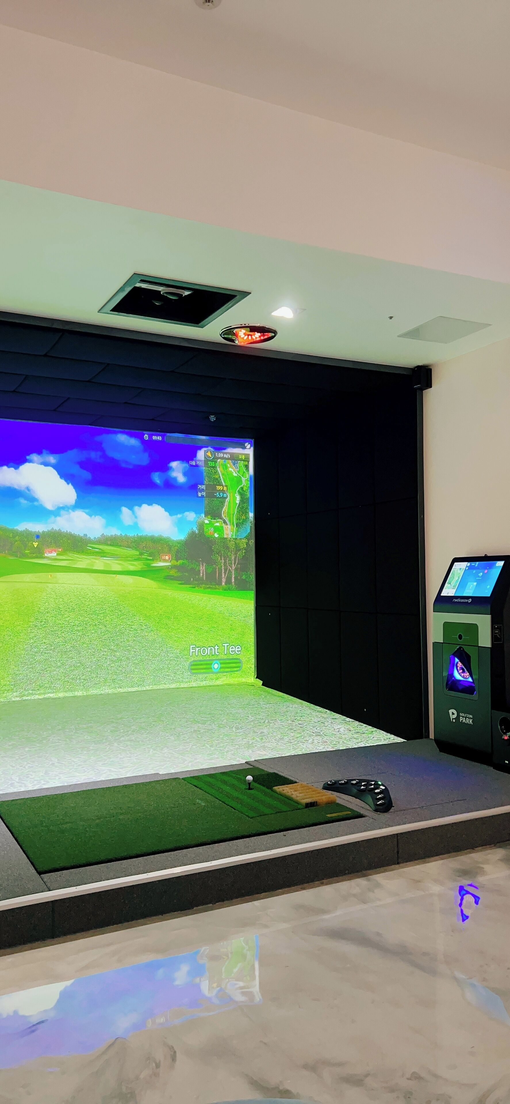 Una habitación con una pantalla grande que muestra un campo de golf, un carrito de golf y un panel de control.