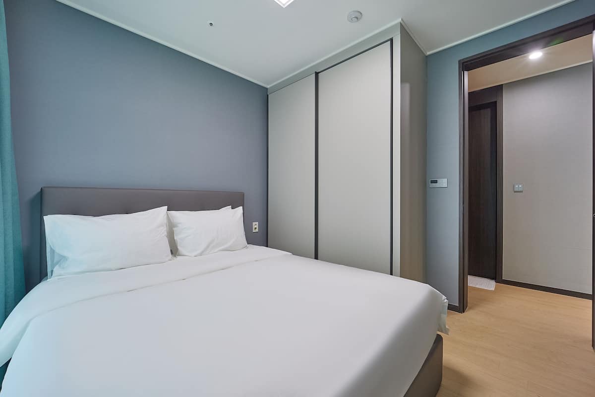 Ein modernes Hotelzimmer mit einem großen Bett, einem Kleiderschrank und einer Tür zu einem weiteren Zimmer.