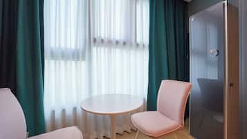 Una habitación con una mesa redonda y dos sillas, una puerta y una ventana con cortinas traslúcidas.