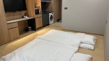 Une chambre de taille modeste, équipée d’un lit, d’un téléviseur fixé au mur, d’un four à micro-ondes et d’un lave-linge.