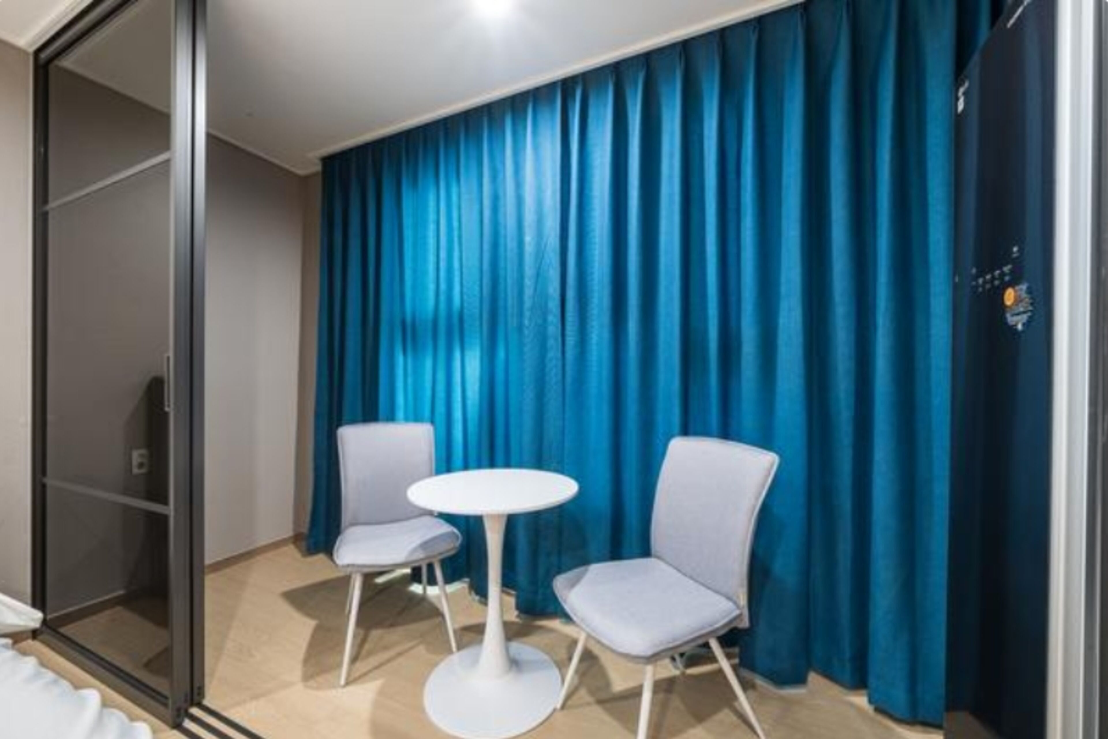 Habitación de hotel con puerta corredera, dos sillas, una mesita redonda y una cortina azul.