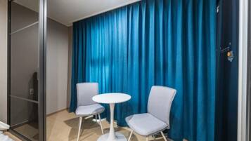 Habitación de hotel con puerta corredera, dos sillas, una mesita redonda y una cortina azul.