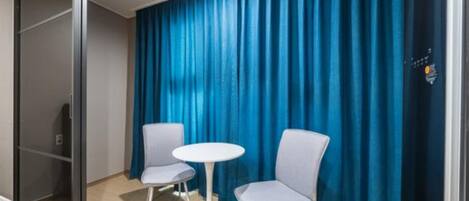 Habitación de hotel con puerta corredera, dos sillas, una mesita redonda y una cortina azul.