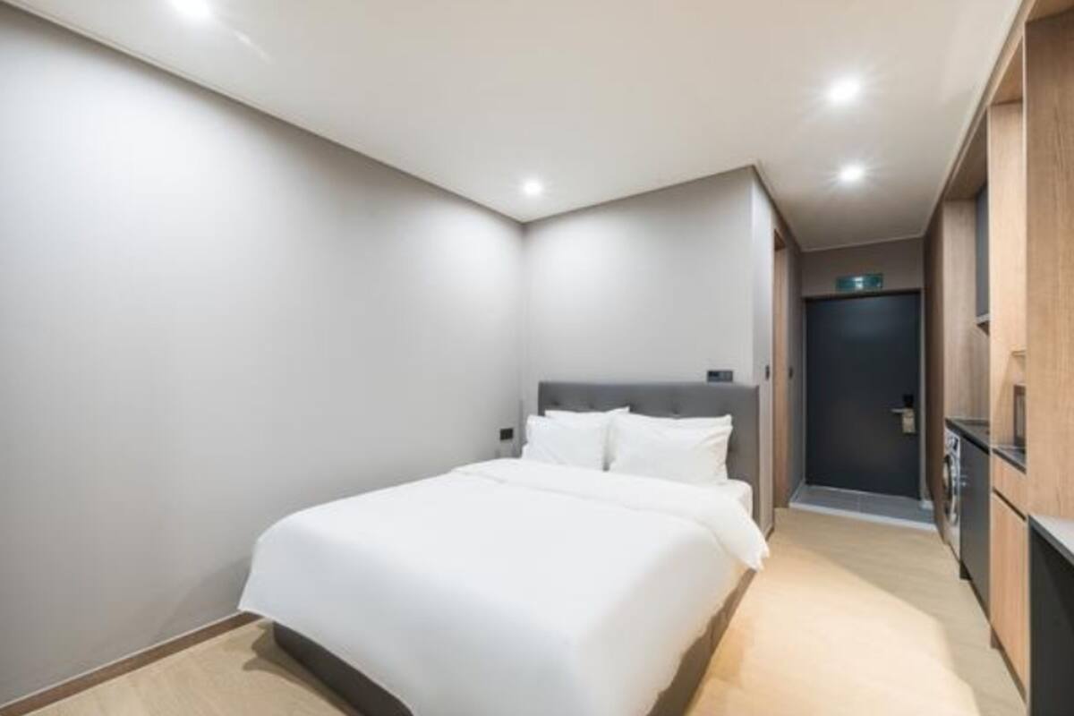 Ein modernes Hotelzimmer mit einem großen Bett, einer kleinen Küchenzeile und einer Tür zu einem Badezimmer.
