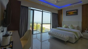 A hotel room with a large bed, a desk with a chair, a television, and a balcony with a view of the beach. - DERA Resort & Spa- Cox's Bazar (Cox's Bazar)