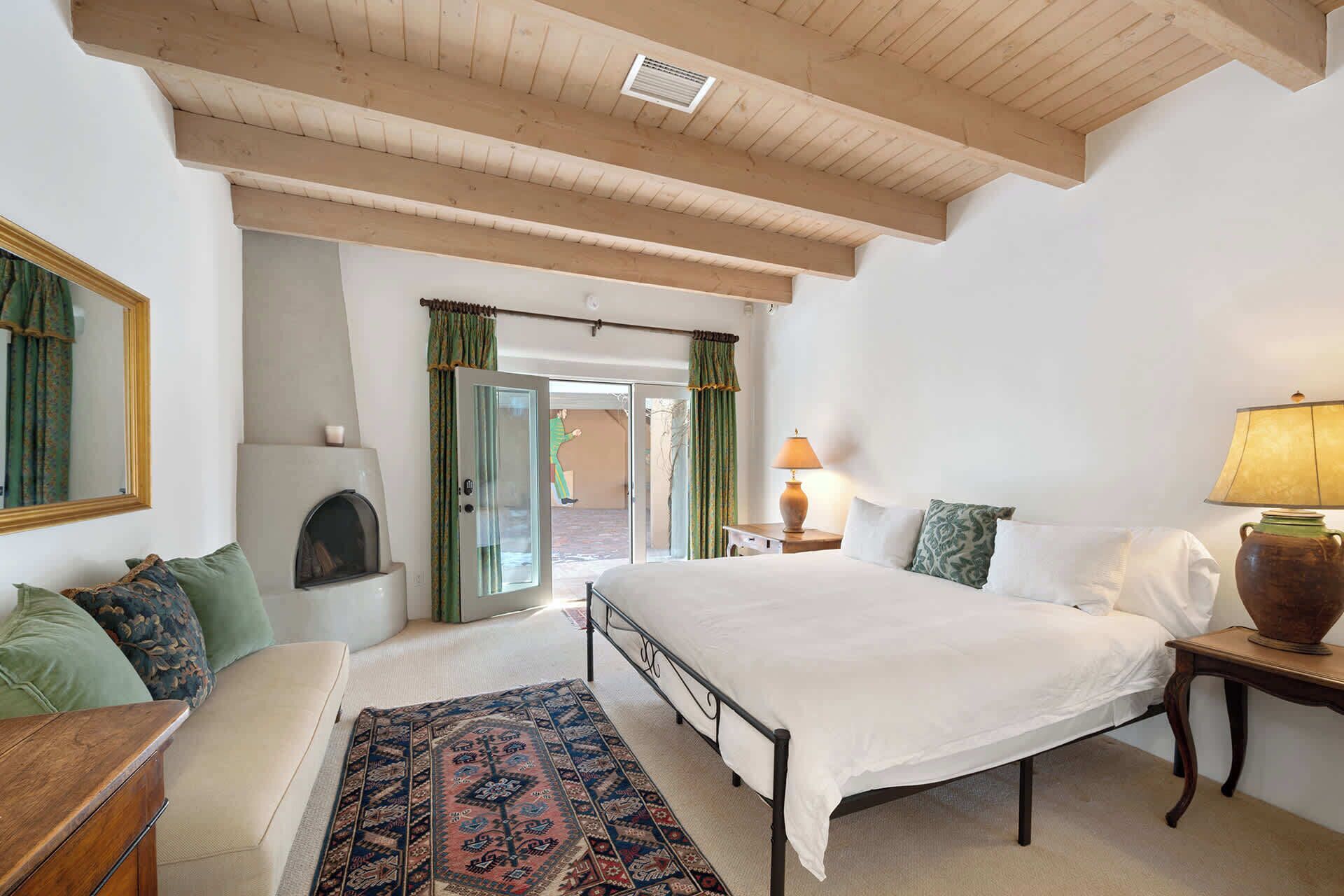 Un dormitorio con una cama grande, techo de madera, chimenea y vistas a través de un ventanal.