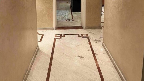 Een gang met beige wanden en een marmeren vloer met geometrische patronen.