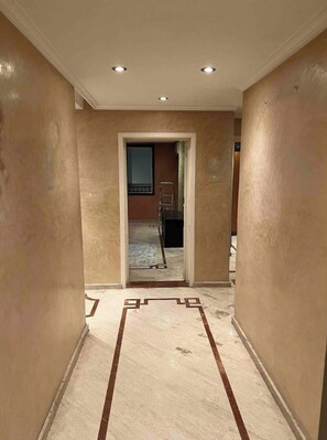 Un couloir aux murs de couleur beige et au sol en marbre orné de motifs géométriques.