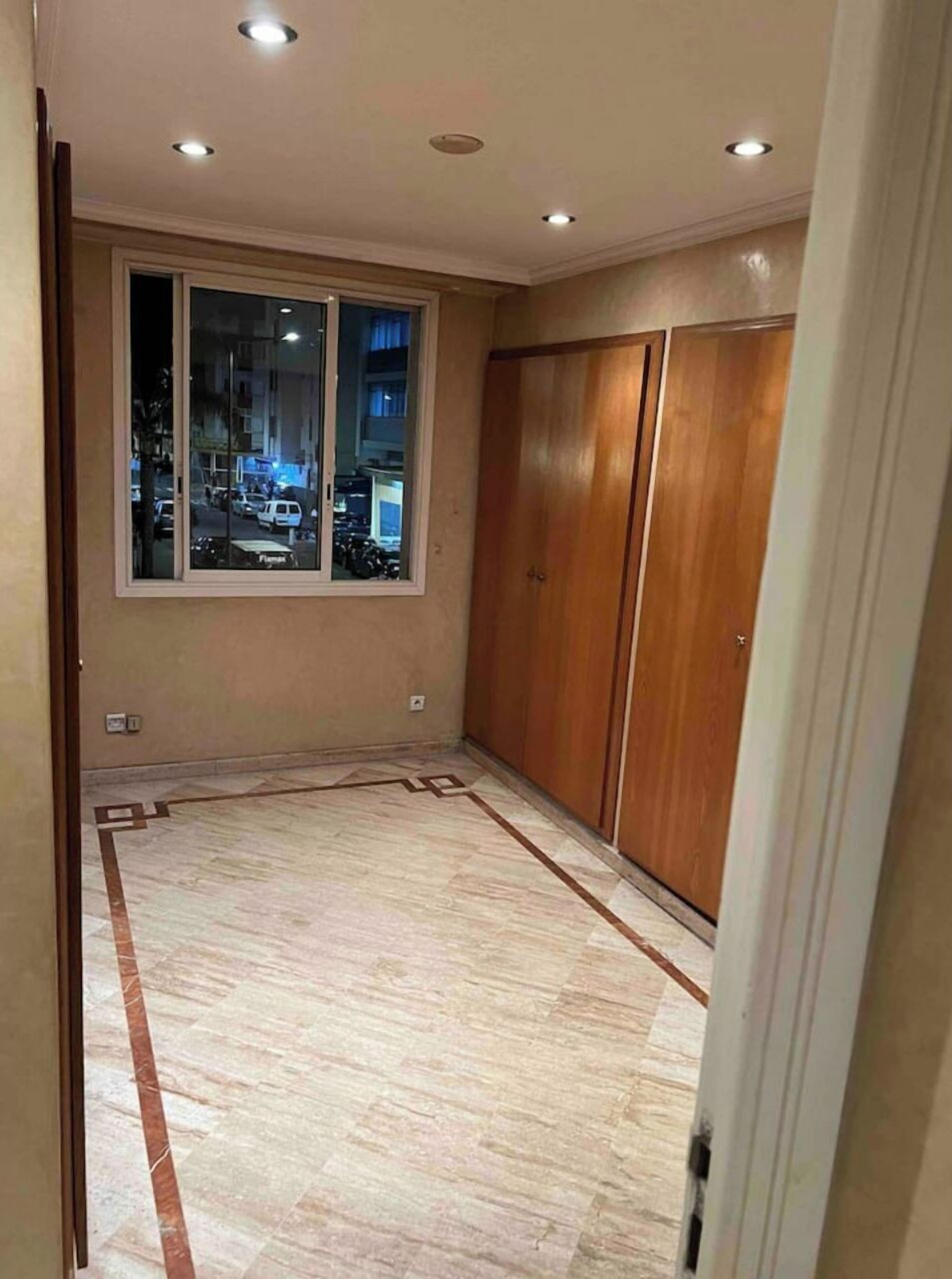 Una habitación con un ventanal grande, un armario de madera y suelo de baldosas.
