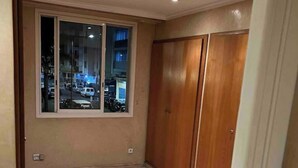 Een kamer met een groot raam, een houten garderobe en een betegelde vloer.