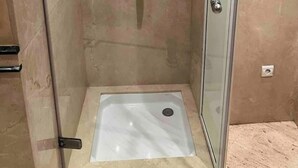 Een kleine, afgesloten douchecel met een glazen deur, een marmeren wand en een enkele kraan.