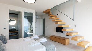 A modern bedroom with a large bed, a built-in bench, a wooden staircase, and a TV mounted on the wall. - Krystallon West - Superb sea views, walking distance to the beach and Paleochora (Chania)