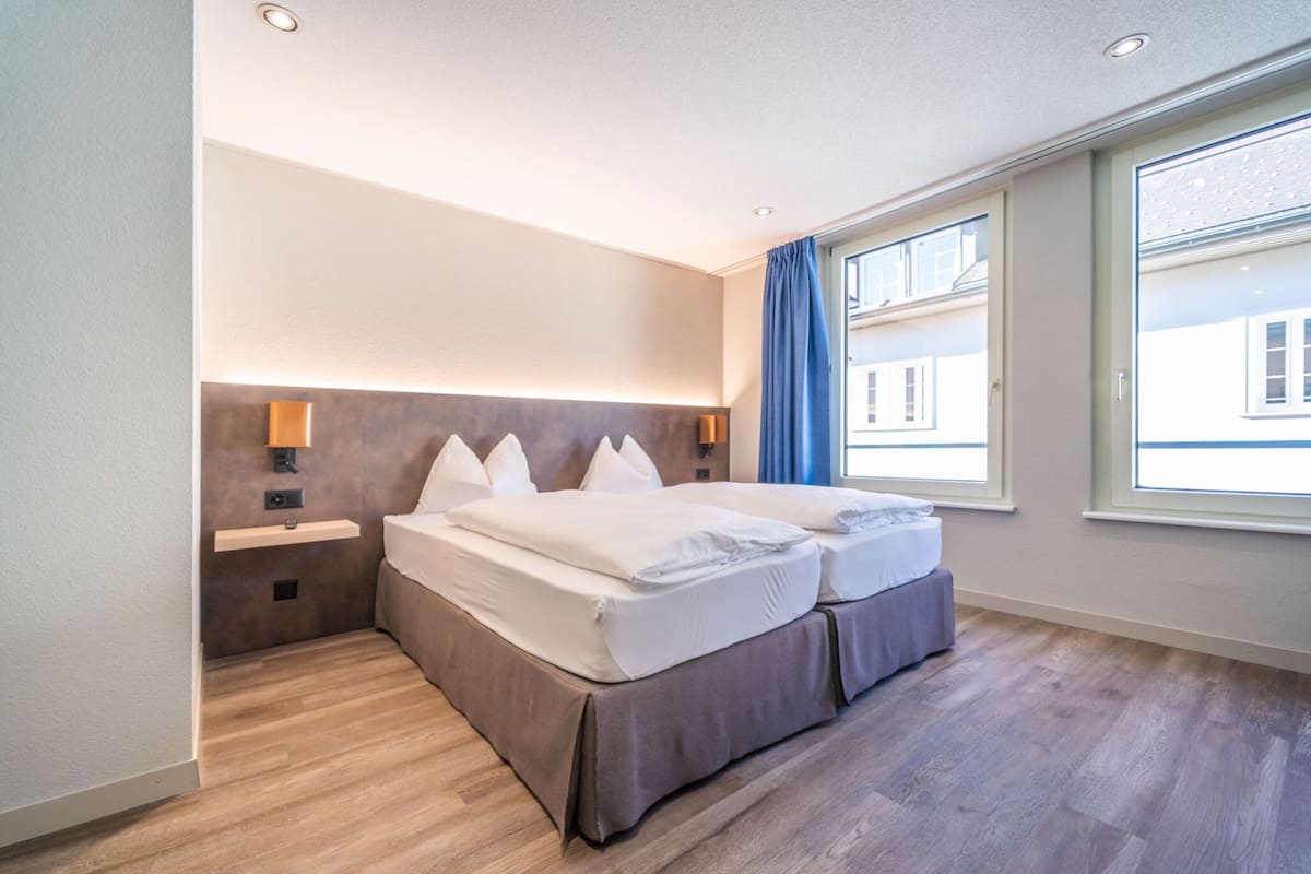 A modern hotel room with a large bed, bedside tables, and a view of the city through the window.