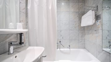 A modern bathroom with a marble-tiled shower, a white bathtub, and a sink with a mirror above it.