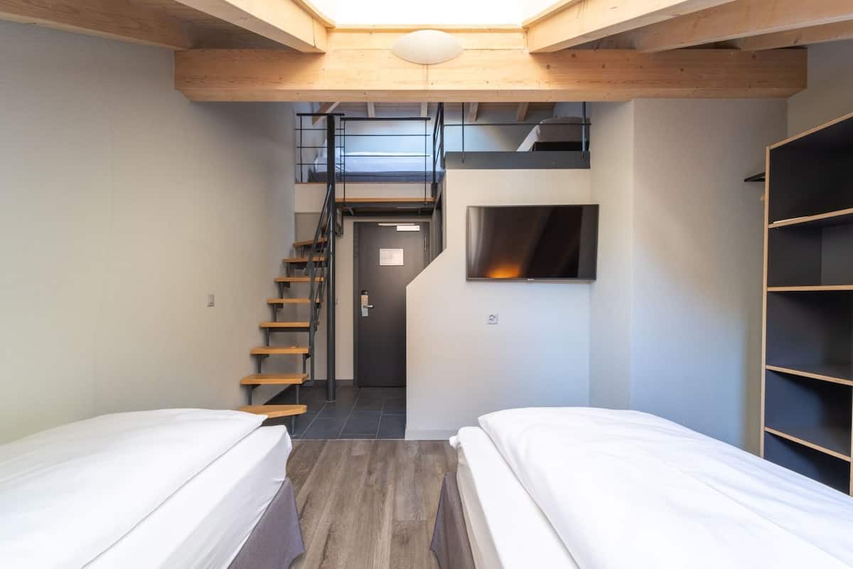 A compact room with two beds, a staircase, a built-in TV, and a wooden ceiling.