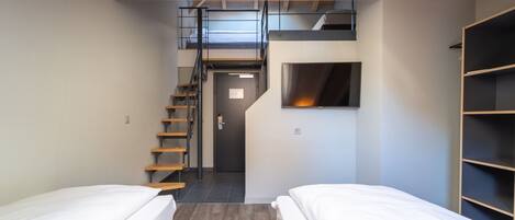 A compact room with two beds, a staircase, a built-in TV, and a wooden ceiling.