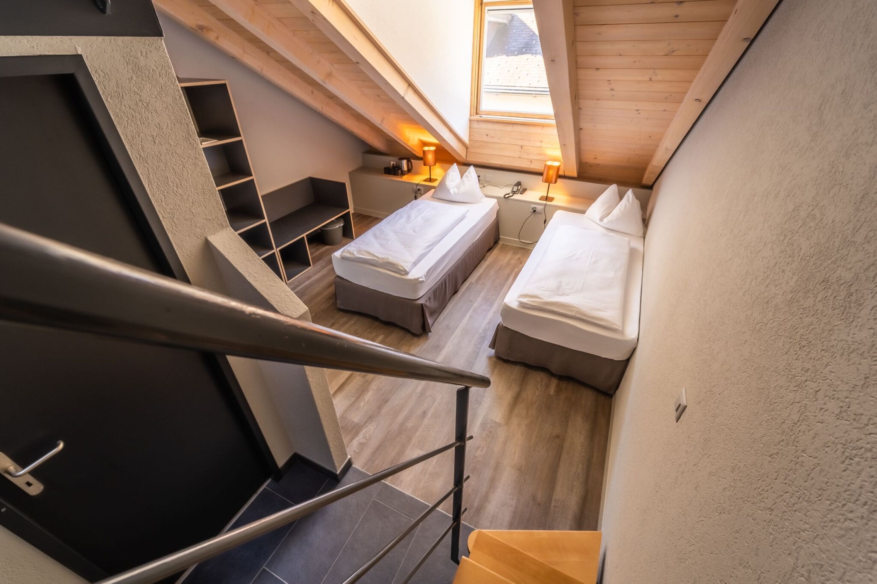 Ein kompakter, moderner Raum mit zwei Betten, einem kleinen Schreibtisch und einem Fenster mit Tageslicht.