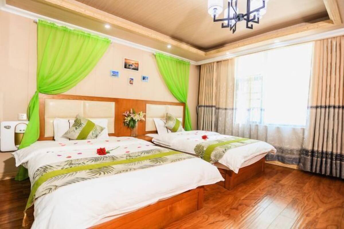 A hotel room with two beds, a wooden headboard, a large window with curtains, and a ceiling light fixture.