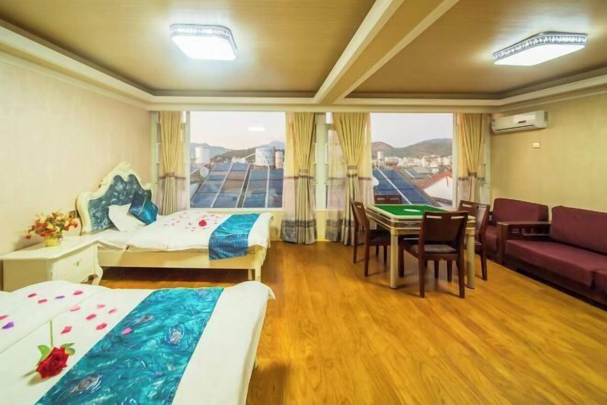 A hotel room with a bed, a dining table, a sofa, and a view of the cityscape.