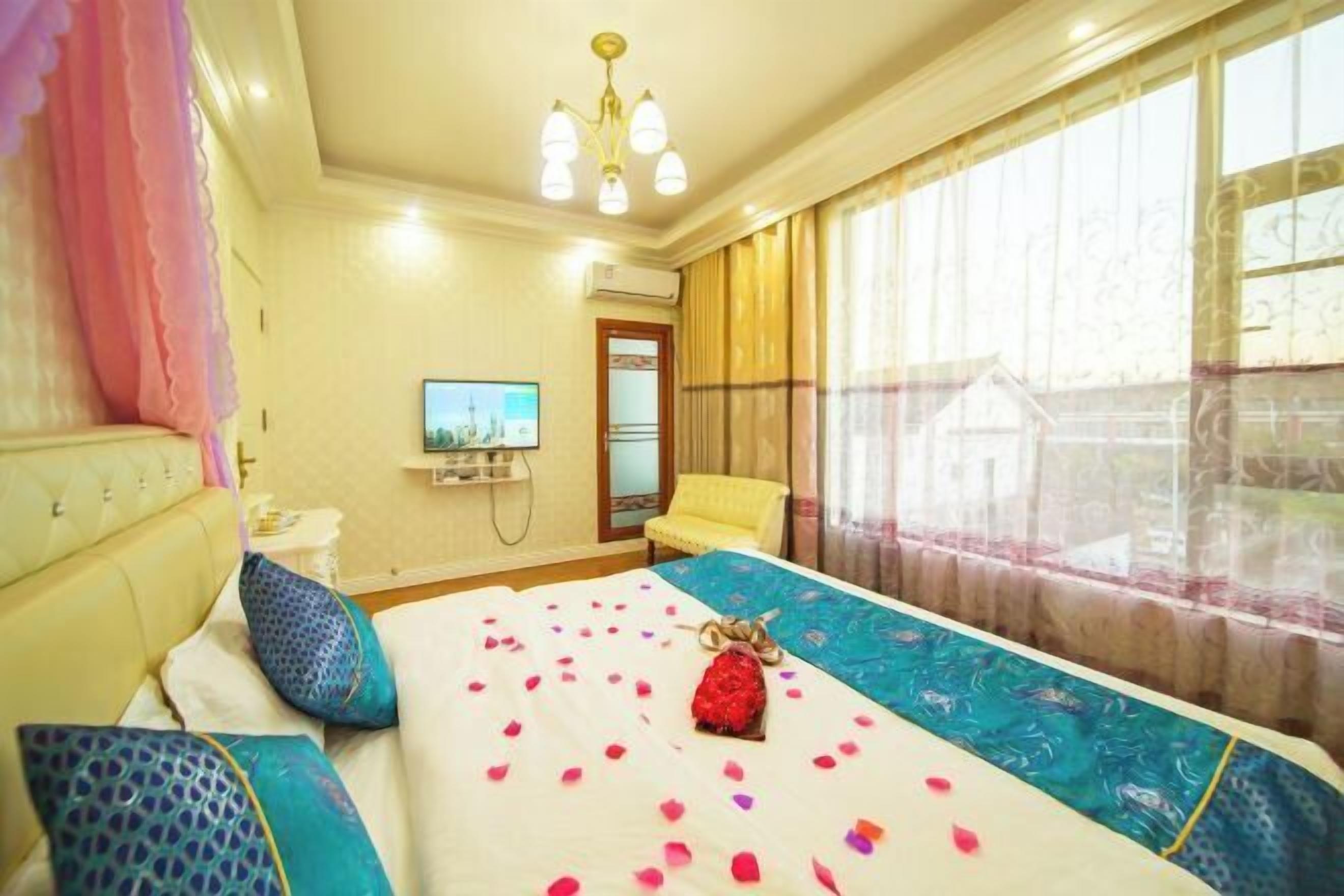 Una habitación de hotel con una cama, televisión, ventana con cortinas y un candelabro.