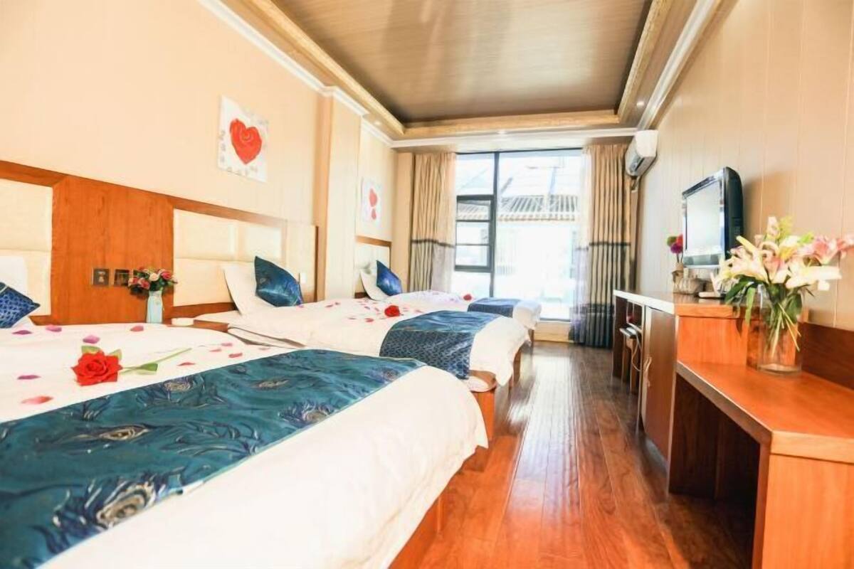 A hotel room with two beds, a desk, a TV, and a window with curtains.