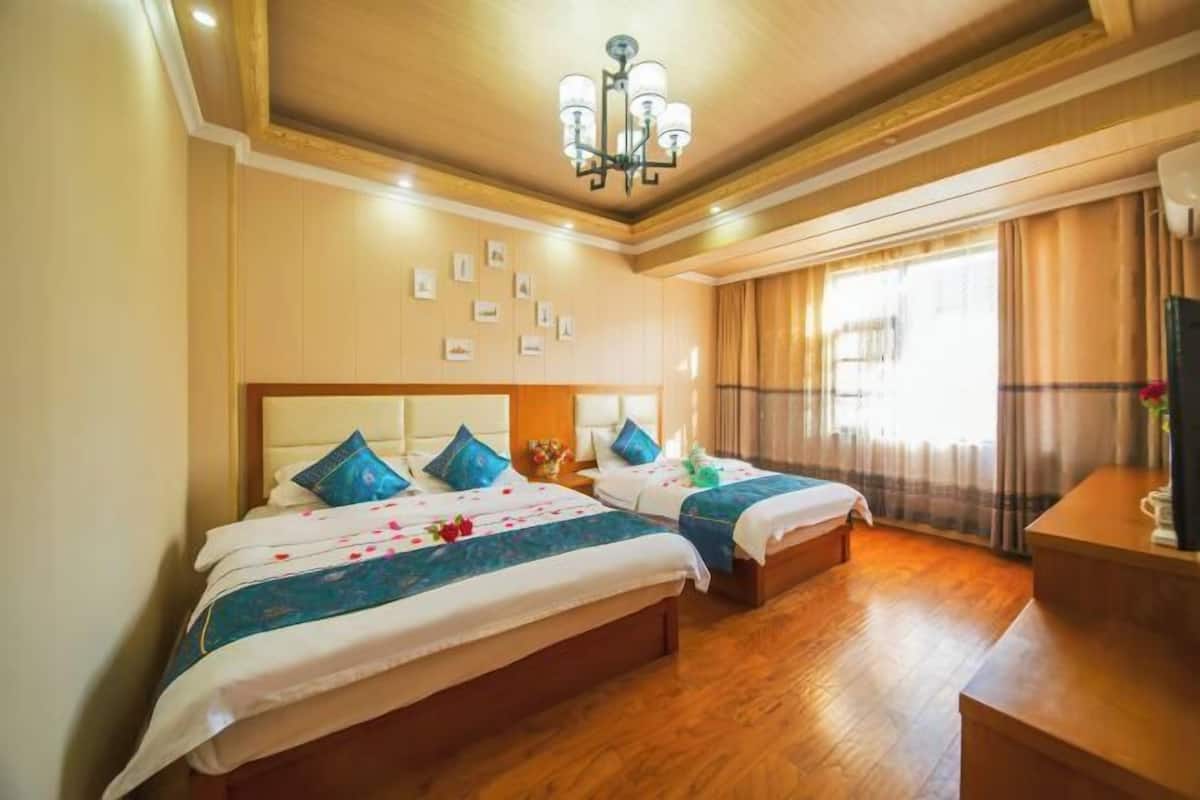 A hotel room with two beds, wooden flooring, a chandelier, and a large window with curtains.