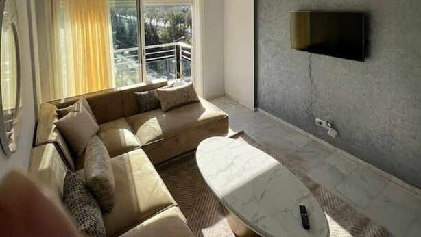 A modern living room with a sectional sofa, a marble coffee table, and a large window offering a view of the outdoors. - Shiny appartment in Prestigia (Rabat)